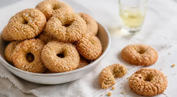 Ciambelline al vino friabilissime, dorate e cosparse di zucchero, in una ciotola e sparse su un panno, con un bicchierino di vino.