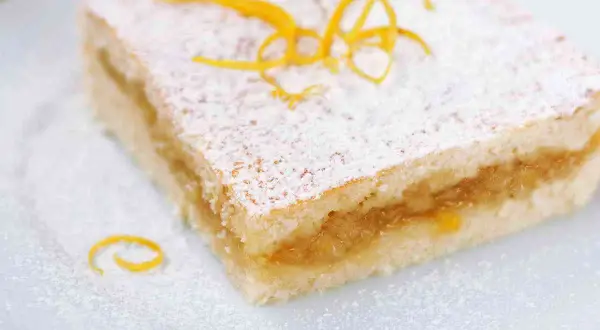 Una fetta di torta con pasta frolla morbida, ripiena di marmellata e spolverata di zucchero a velo e scorza d'arancia.