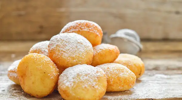 Pile di frittelle di zucca dorate e soffici, cosparse di zucchero a velo, su un tavolo di legno rustico.