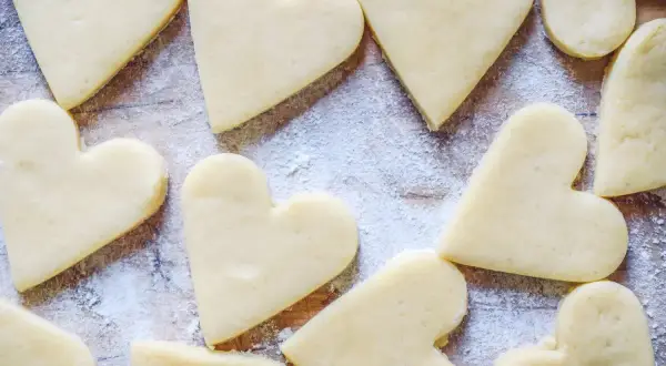 Cuore di biscotti senza burro spolverati di zucchero a velo su un tagliere di legno.