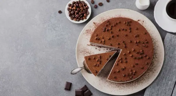 Una deliziosa torta al caffè, cosparsa di cacao e gocce di cioccolato, con una fetta servita. Chicchi di caffè e cioccolato completano la scena.