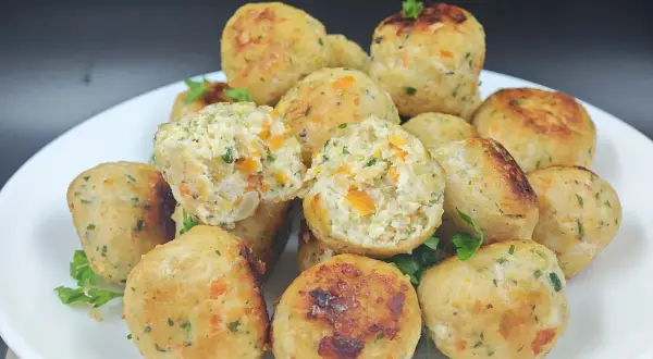 Un piatto di polpette di pollo dorate, con pezzetti di carota e prezzemolo visibili all'interno. Alcune sono leggermente aperte, mostrando la morbidezza.
