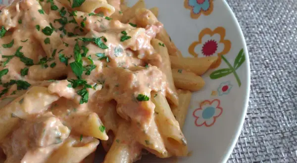 Penne al baffo cremose e saporite, condite con una salsa rosa e prezzemolo fresco, servite su un piatto decorato con fiori.