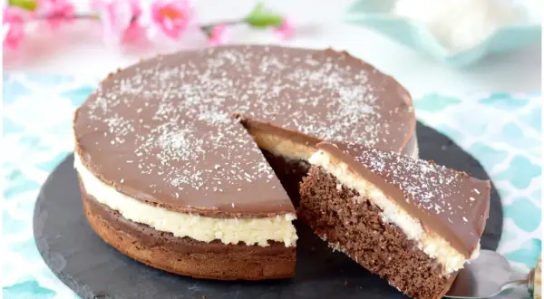 Deliziosa torta cocco e cioccolato, con una fetta appena tagliata, cosparsa di cocco grattugiato.