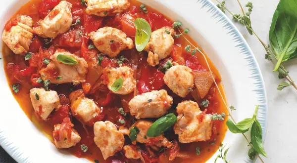 Piatto di coniglio alla cacciatora ricetta della nonna, con pezzi di carne tenera in salsa di pomodoro e peperoni, guarnito con basilico fresco e timo.