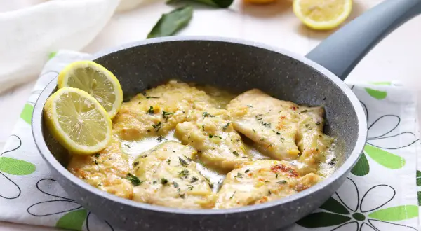 Scaloppine al limone cremose in padella, guarnite con spicchi di limone fresco e prezzemolo tritato.
