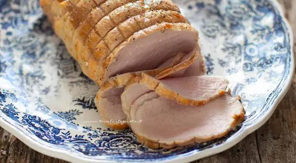 Arrosto di maiale morbido con sughetto, affettato su un piatto decorato con motivi blu. Perfetto per un pranzo domenicale.