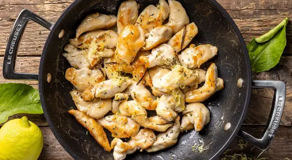 Pezzetti di petto di pollo dorati in padella, conditi con limone e erbe aromatiche. Un'idea veloce per le tue ricette di petto di pollo.