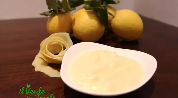 Una ciotola di cremosa crema al limone, con limoni freschi e una decorazione a forma di rosa fatta con la scorza.