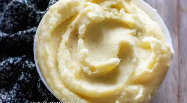Una ciotola di cremoso pure di patate, guarnito con pepe nero macinato, su un tessuto scuro.