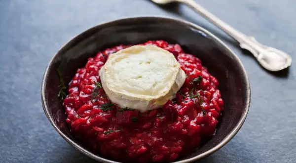 Un cremoso risotto alla barbabietola, con una fetta di formaggio di capra fuso sopra e un rametto di erbe aromatiche.
