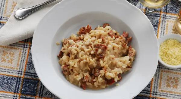 Un piatto di risotto alla pilota cremoso, con pezzetti di salsiccia, servito su una tovaglia a quadri.