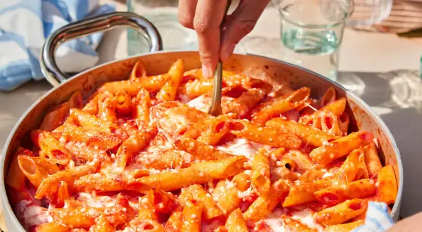 Un primo piatto invitante: pasta alla sorrentina fumante, con pomodoro e mozzarella filante, pronta per essere servita.
