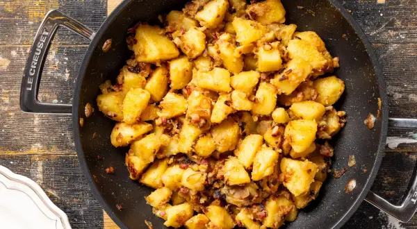 Patate in tecia dorate e croccanti, con pezzetti di pancetta e cipolla, pronte per essere gustate.