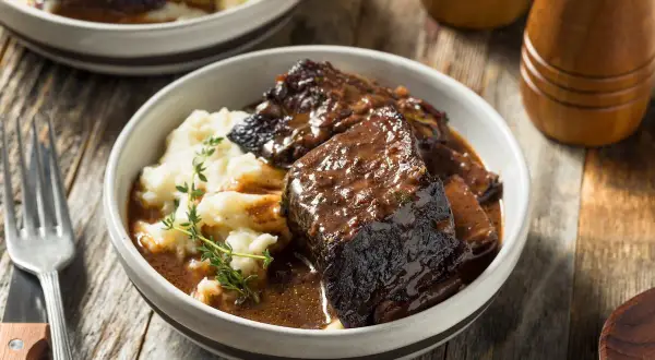 Un succulento brasato di manzo servito con purè di patate e guarnito con timo fresco.
