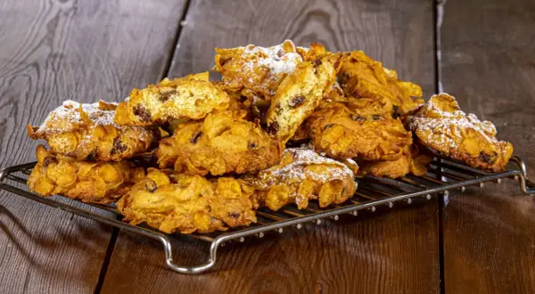Biscotti croccanti, simili a rose del deserto, con uvetta e fiocchi di mais, spolverati di zucchero a velo su una griglia metallica.