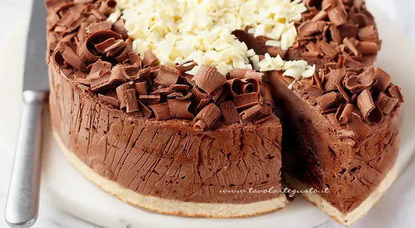 Delizioso semifreddo al cioccolato, ricoperto di riccioli di cioccolato fondente e bianco. Una fetta è stata tagliata, rivelando la sua consistenza cremosa.