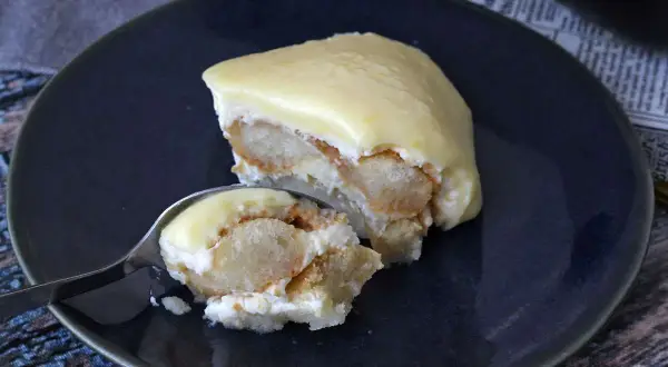 Una fetta di tiramisù al limone su un piatto blu, con un cucchiaino che ne preleva un assaggio.