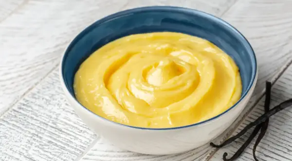 Una ciotola di cremosa crema pasticcera classica, con baccelli di vaniglia scuri accanto.