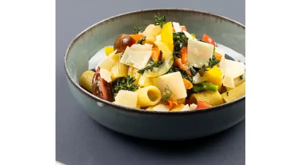 Piatto di pasta con verdure fresche, pomodorini, peperoni gialli e scaglie di parmigiano.