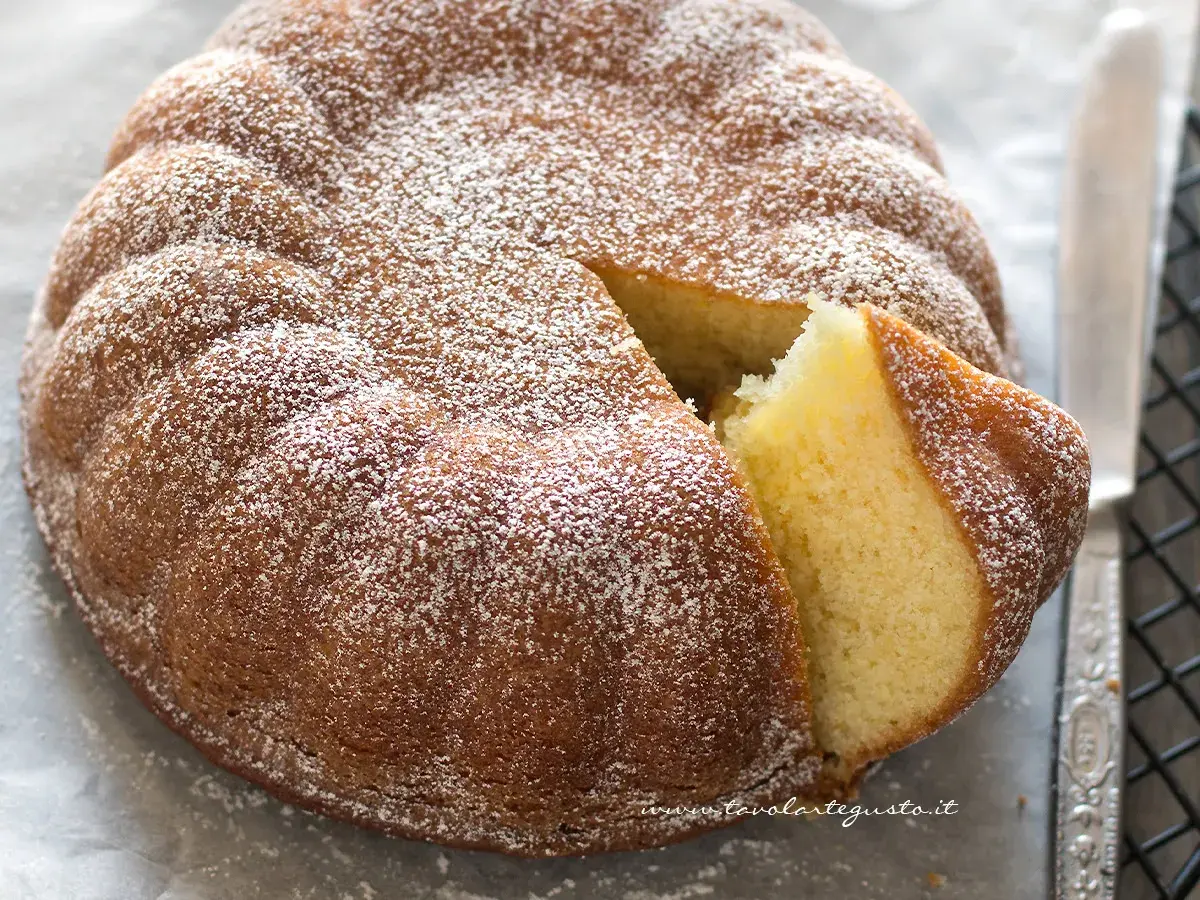 Una torta semplice e veloce, soffice e spolverata di zucchero a velo, con una fetta tagliata che ne mostra l'interno dorato.