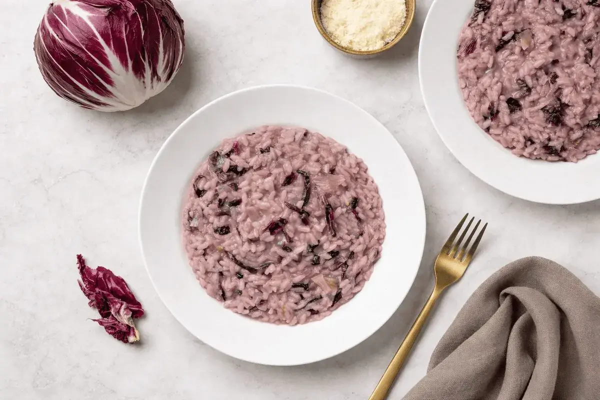 Un cremoso risotto al radicchio rosso, con un cespo intero e foglie sparse, pronto per essere gustato.