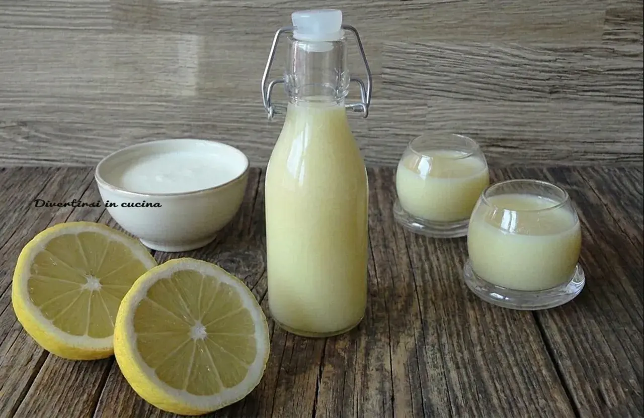 Una bottiglia e due bicchierini di crema di limoncello, con limoni freschi e una ciotola di panna.