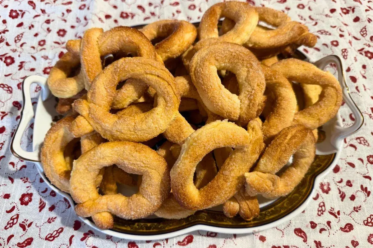 Un piatto pieno di torcetti al burro, dorati e zuccherati, pronti per essere gustati.
