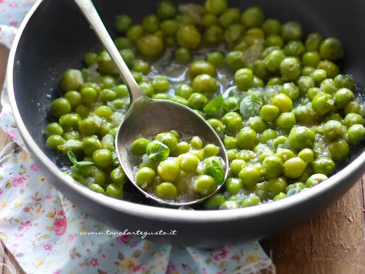 Piselli freschi in padella, cotti con cipolla e menta. Un cucchiaio ne raccoglie una porzione invitante.