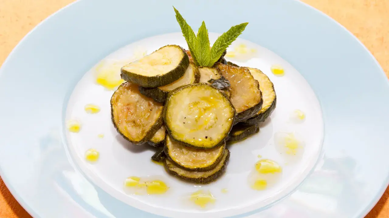 Fette di zucchine alla scapece, condite con olio e guarnite con menta fresca, su un piatto bianco.