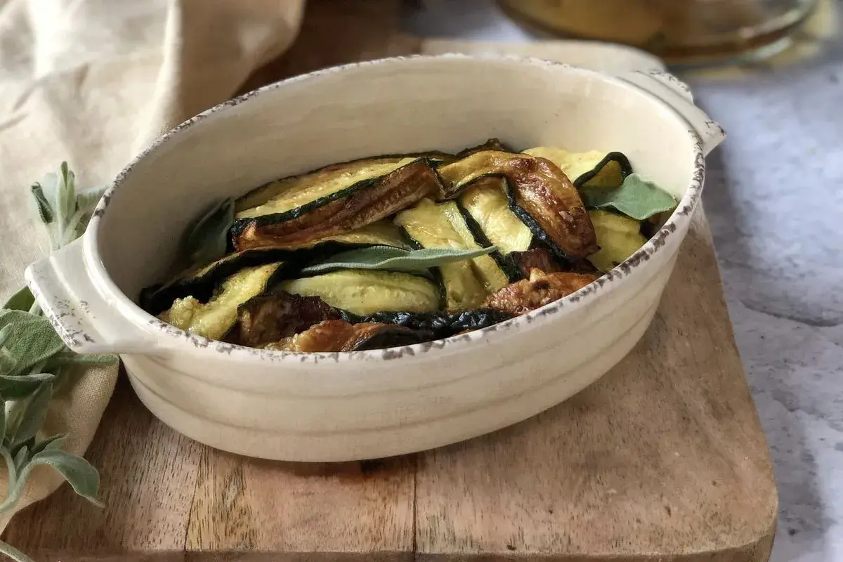Zucchine in carpione dorate e saporite, guarnite con foglie di salvia fresca, servite in una ciotola rustica.
