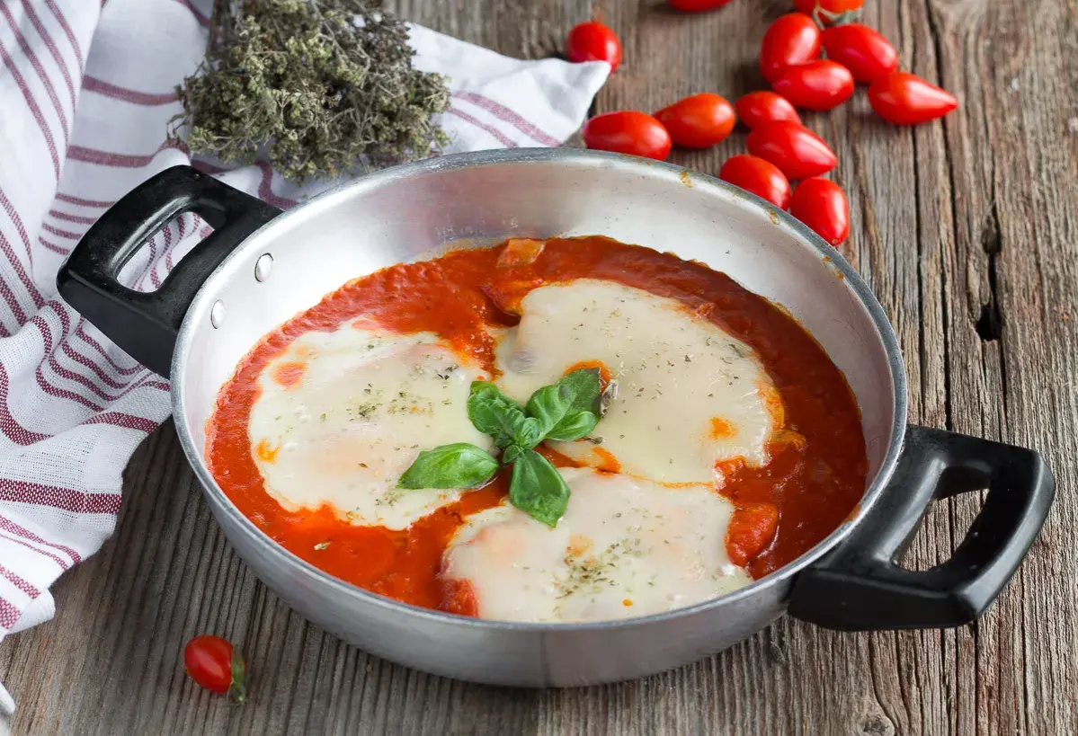 Un invitante pollo alla pizzaiola in padella, con mozzarella filante e basilico fresco, pronto per essere gustato.