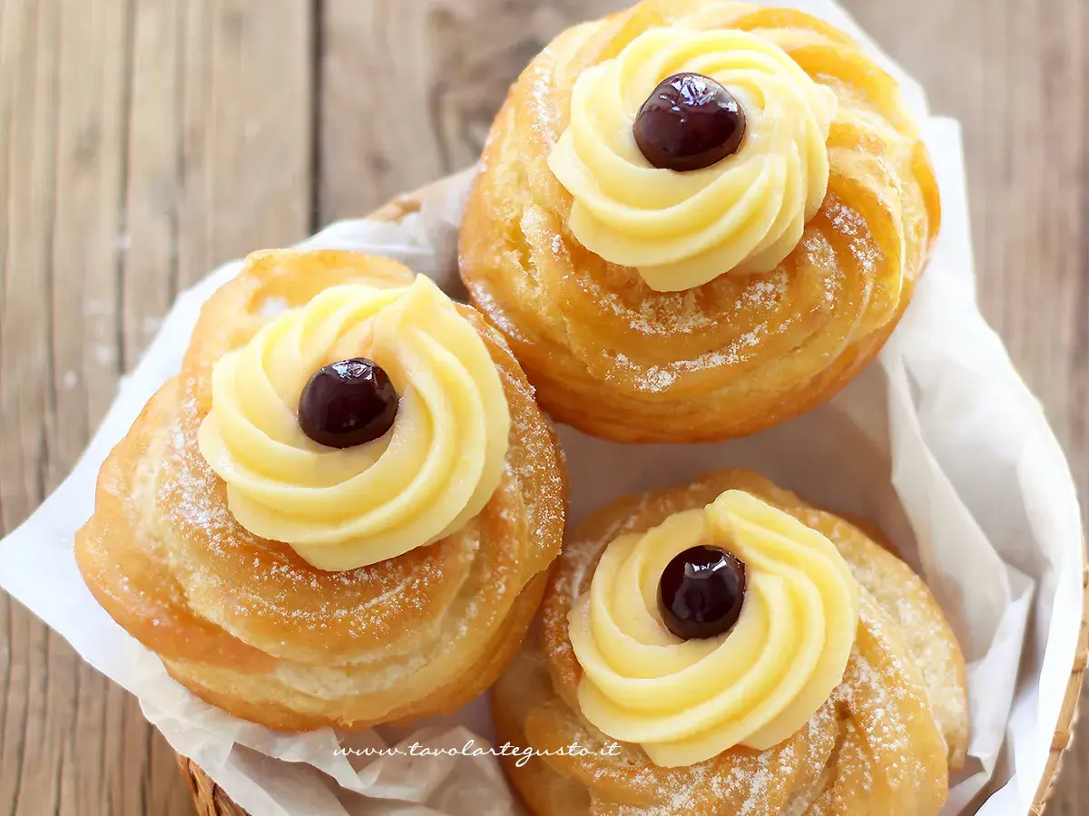 Tre zeppole di San Giuseppe, dolci fritti con crema pasticcera e ciliegina, spolverate di zucchero a velo.