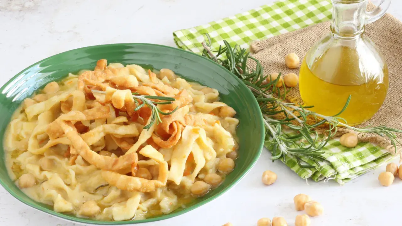 Piatto di ciceri e tria, pasta fresca con ceci, guarnito con rosmarino e croccanti straccetti fritti. Olio d'oliva e ceci sparsi intorno.