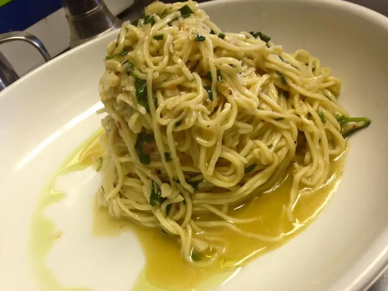 Un piatto di spaghetti aglio olio e peperoncino cremosi, conditi con prezzemolo fresco e un filo d'olio d'oliva, serviti in una ciotola bianca.