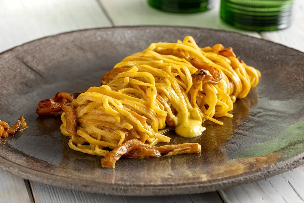 Un piatto di spaghetti con funghi e una cremosa salsa gialla, un esempio di ricette pasta gustose che invitano a scoprire nuovi sapori.