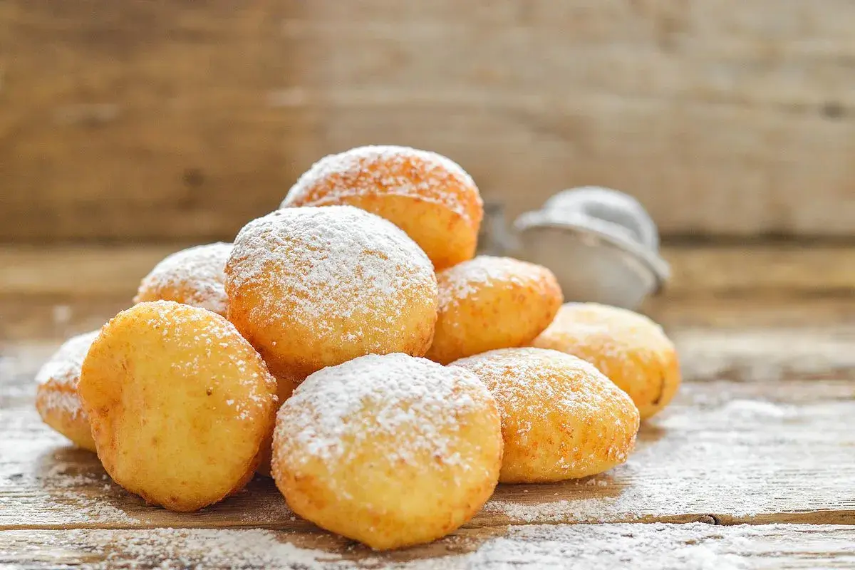 Pile di frittelle di zucca dorate e soffici, cosparse di zucchero a velo, su un tavolo di legno rustico.