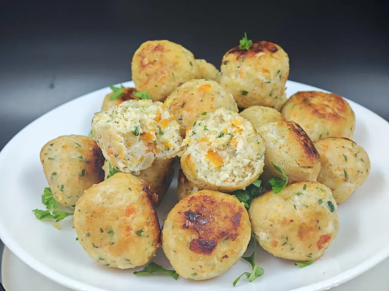 Un piatto di polpette di pollo dorate, con pezzetti di carota e prezzemolo visibili all'interno. Alcune sono leggermente aperte, mostrando la morbidezza.