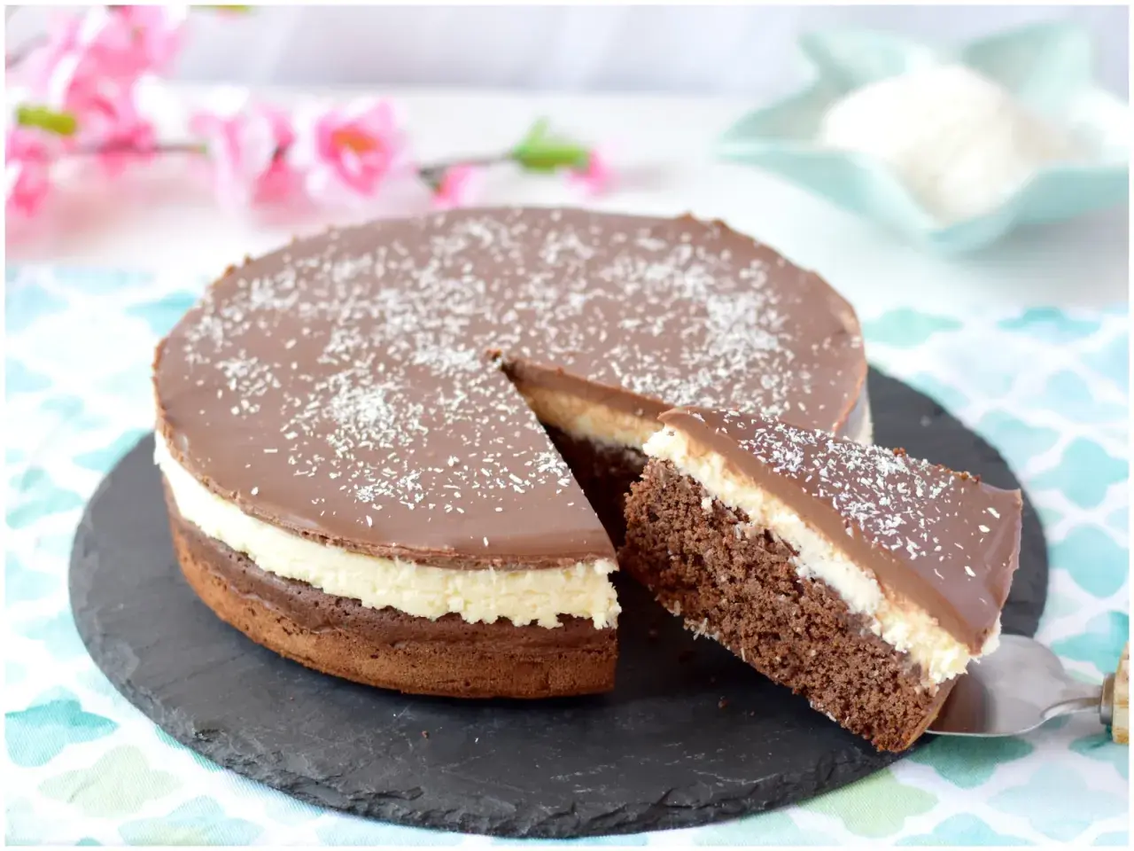 Deliziosa torta cocco e cioccolato, con una fetta appena tagliata, cosparsa di cocco grattugiato.