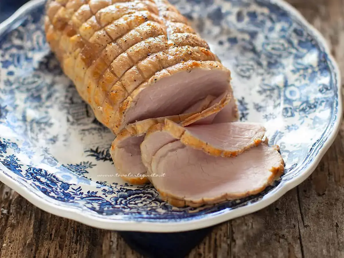 Arrosto di maiale morbido con sughetto, affettato su un piatto decorato con motivi blu. Perfetto per un pranzo domenicale.