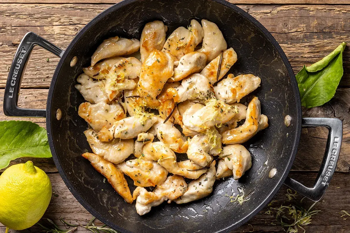 Pezzetti di petto di pollo dorati in padella, conditi con limone e erbe aromatiche. Un'idea veloce per le tue ricette di petto di pollo.