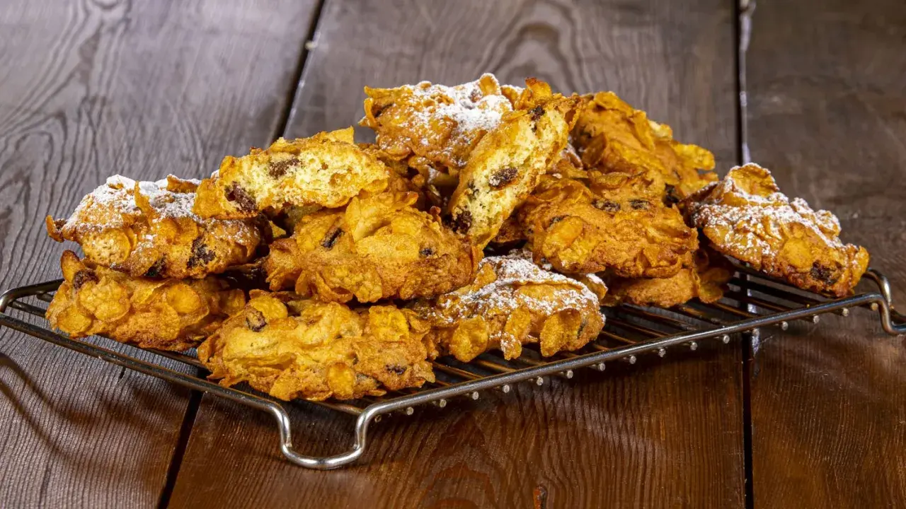 Biscotti croccanti, simili a rose del deserto, con uvetta e fiocchi di mais, spolverati di zucchero a velo su una griglia metallica.
