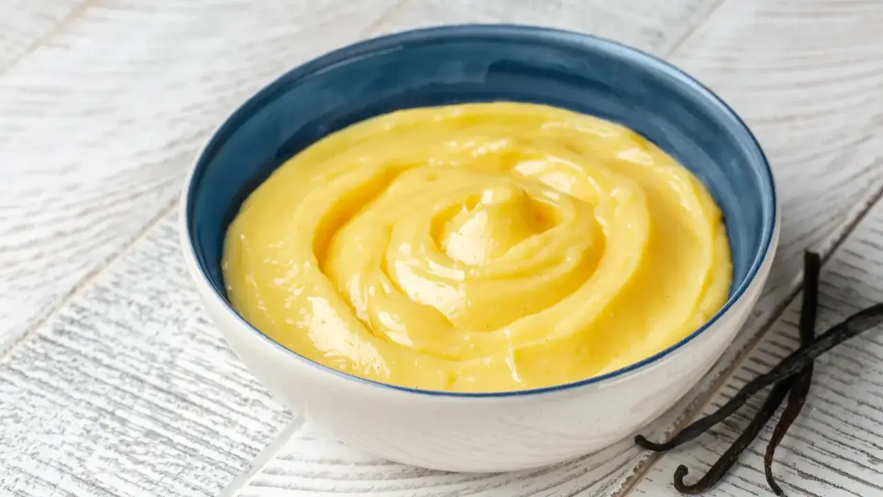 Una ciotola di cremosa crema pasticcera classica, con baccelli di vaniglia scuri accanto.