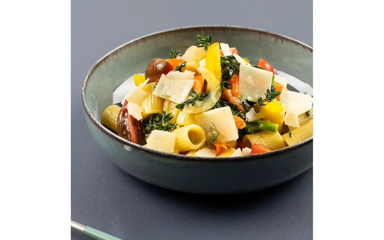 Piatto di pasta con verdure fresche, pomodorini, peperoni gialli e scaglie di parmigiano.