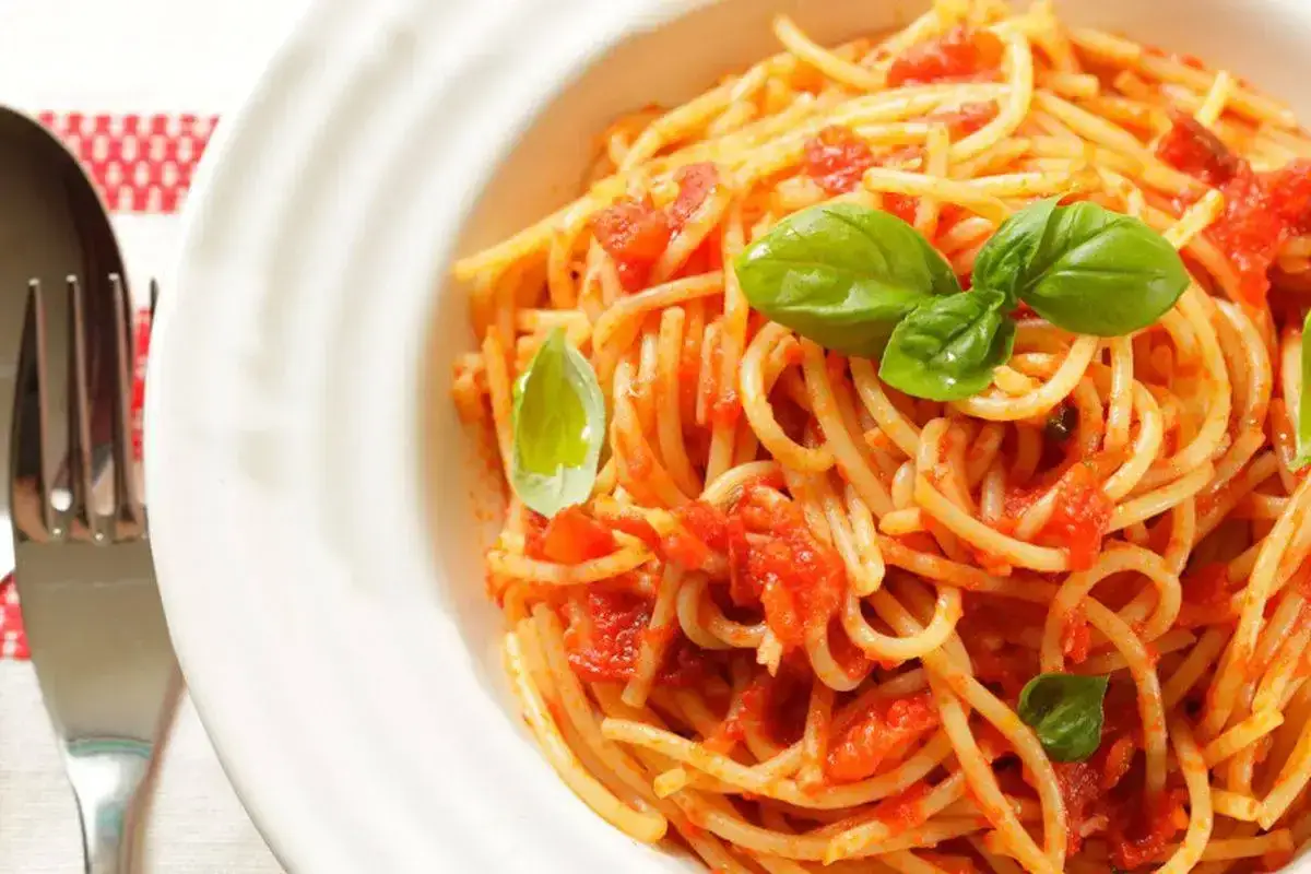 Spaghetti al dente conditi con un sugo fresco di pomodorini e basilico, serviti in un piatto bianco.