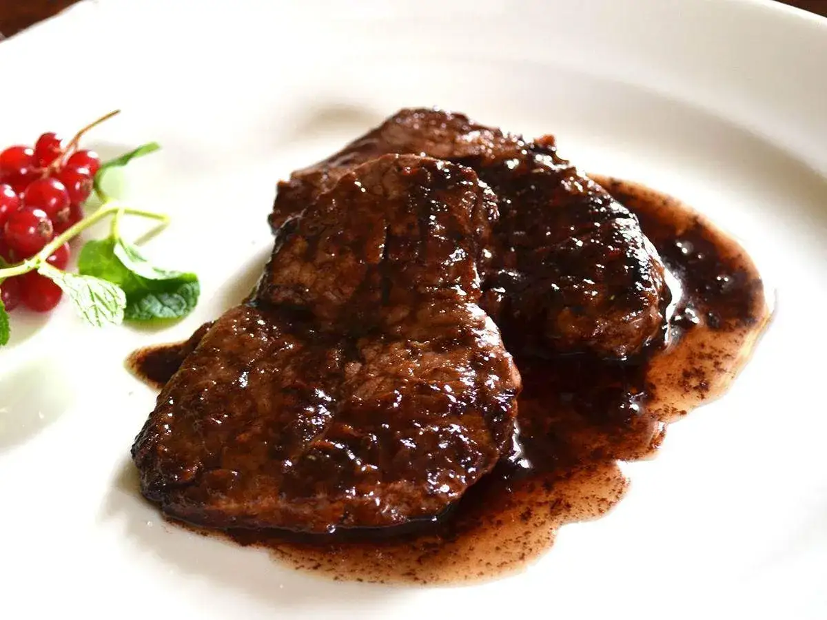Succulento brasato di manzo in salsa scura, guarnito con ribes rossi e menta fresca.