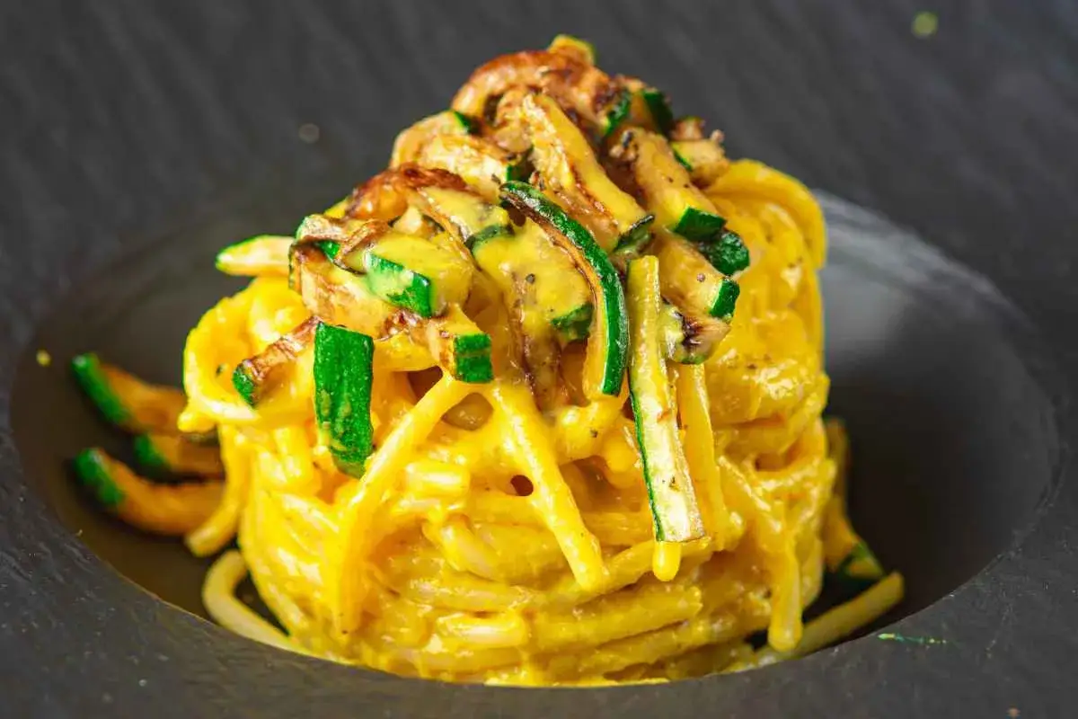 Un piatto di spaghetti conditi con una cremosa salsa gialla, guarnito con zucchine a julienne e funghi croccanti. Una deliziosa carbonara di zucchine.