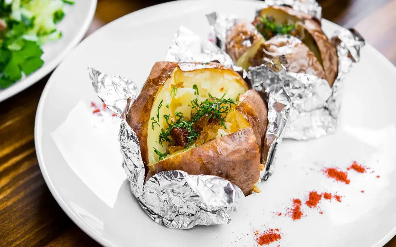 Patate al cartoccio fumanti, condite con erbe fresche e un pizzico di paprika sul piatto bianco.