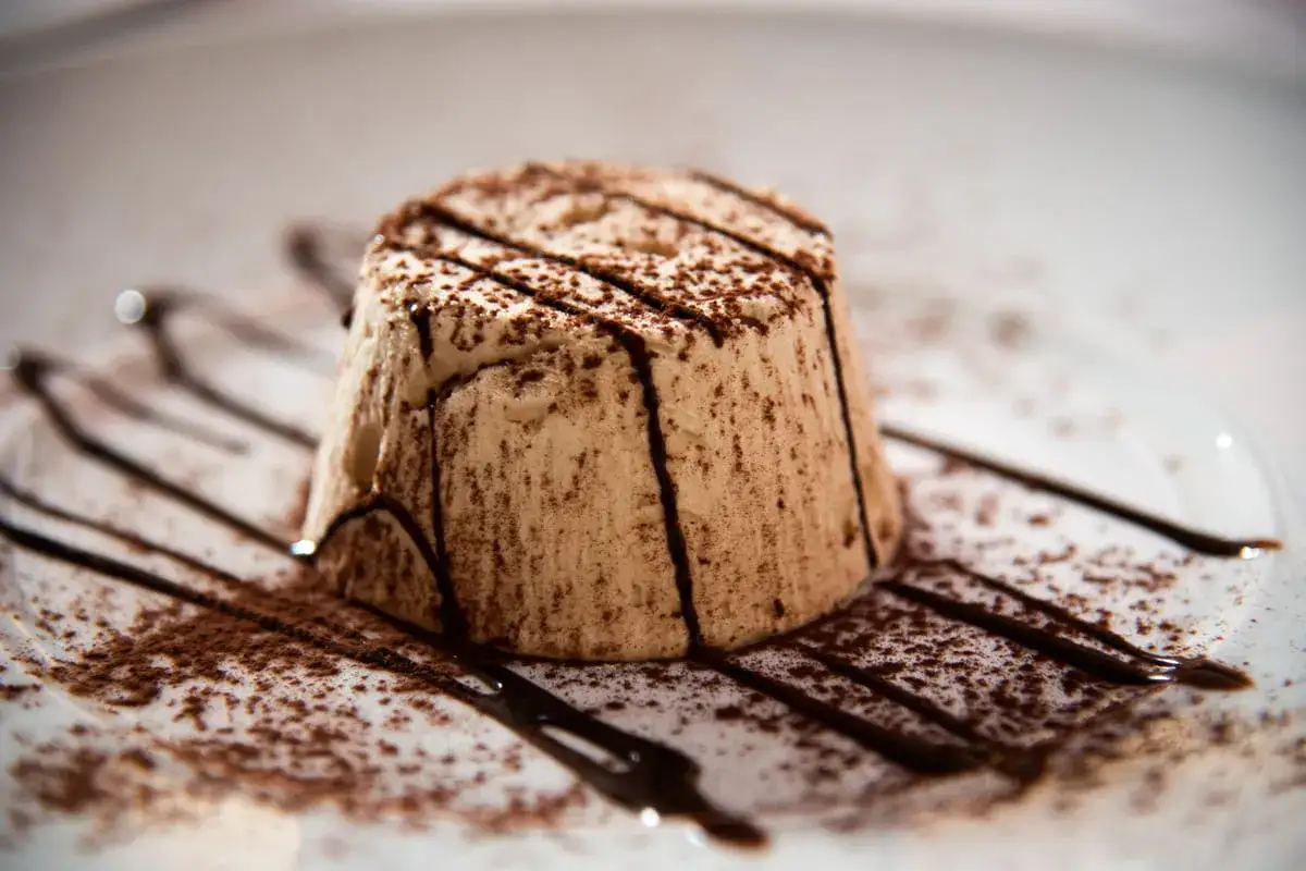 Delizioso parfait di mandorle, spolverato di cacao e decorato con sciroppo al cioccolato su un piatto bianco.