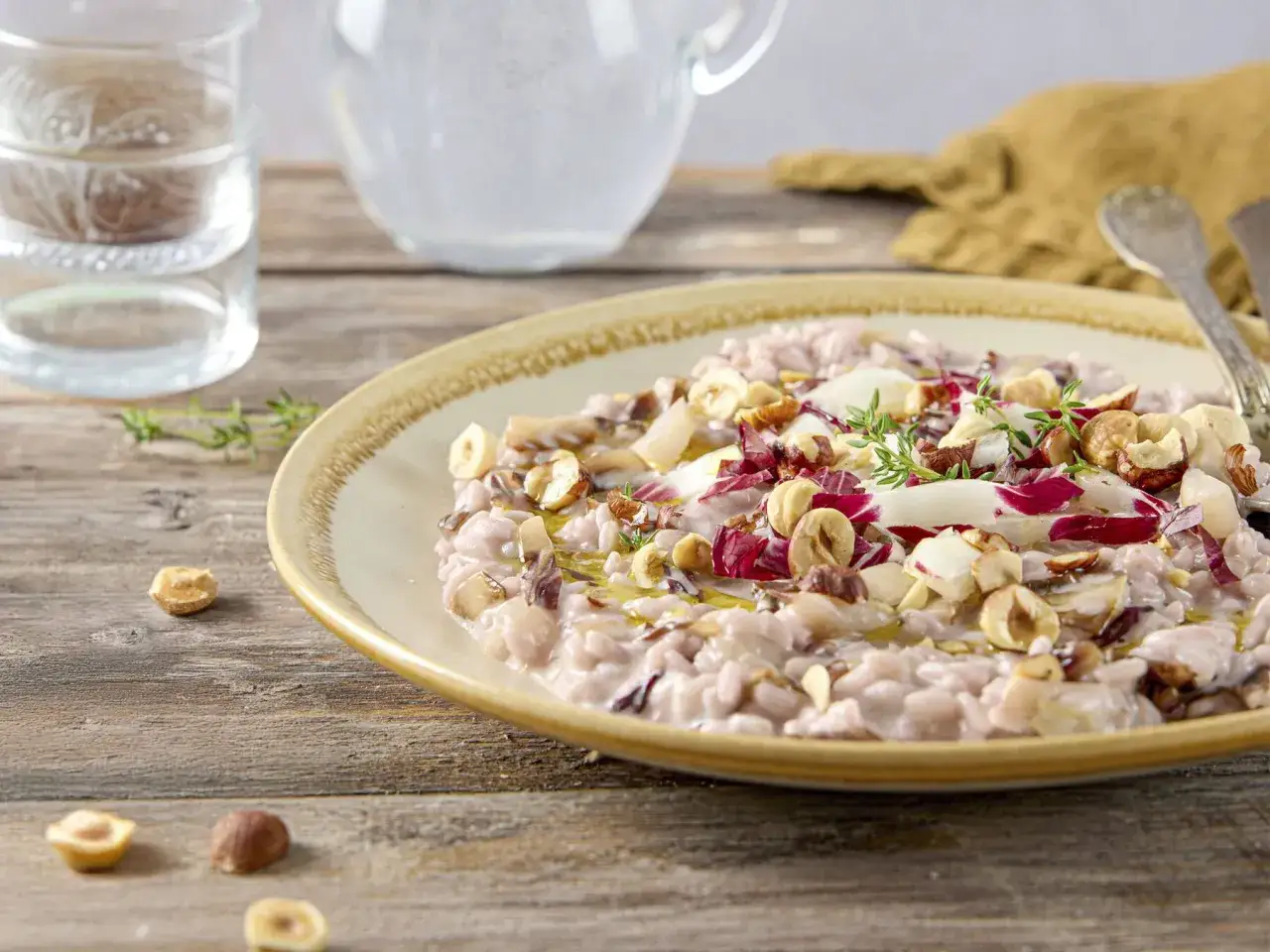 Un cremoso risotto al radicchio rosso, guarnito con nocciole tostate e scaglie di formaggio.
